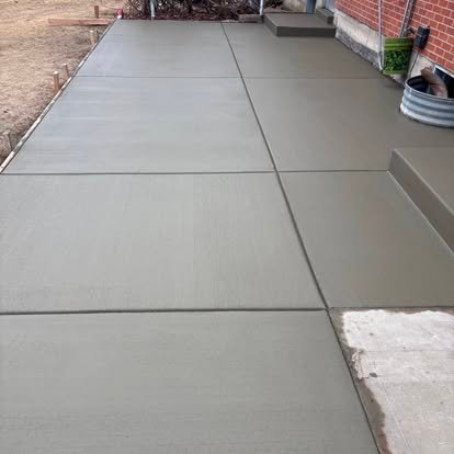 Freshly poured concrete walkway — smooth brushed finish with clean expansion joints next to brick exterior