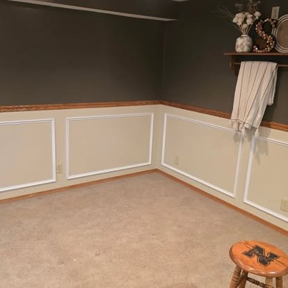 Completed wainscoting installation — white raised panel trim with dark grey accent walls and styled decor